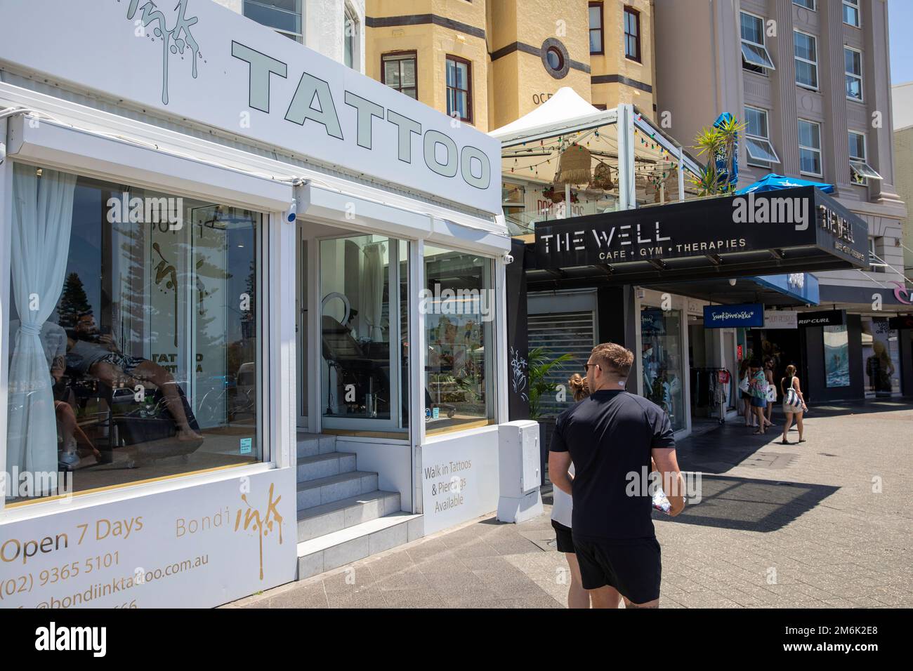 Bondi Ink Tattoo Salon und der Brunnen Gym und Cafe, campbell Parade, Bondi Beach. Ein Mann am Telefon, während er tätowiert wurde, Sydney, NSW, Australien Stockfoto