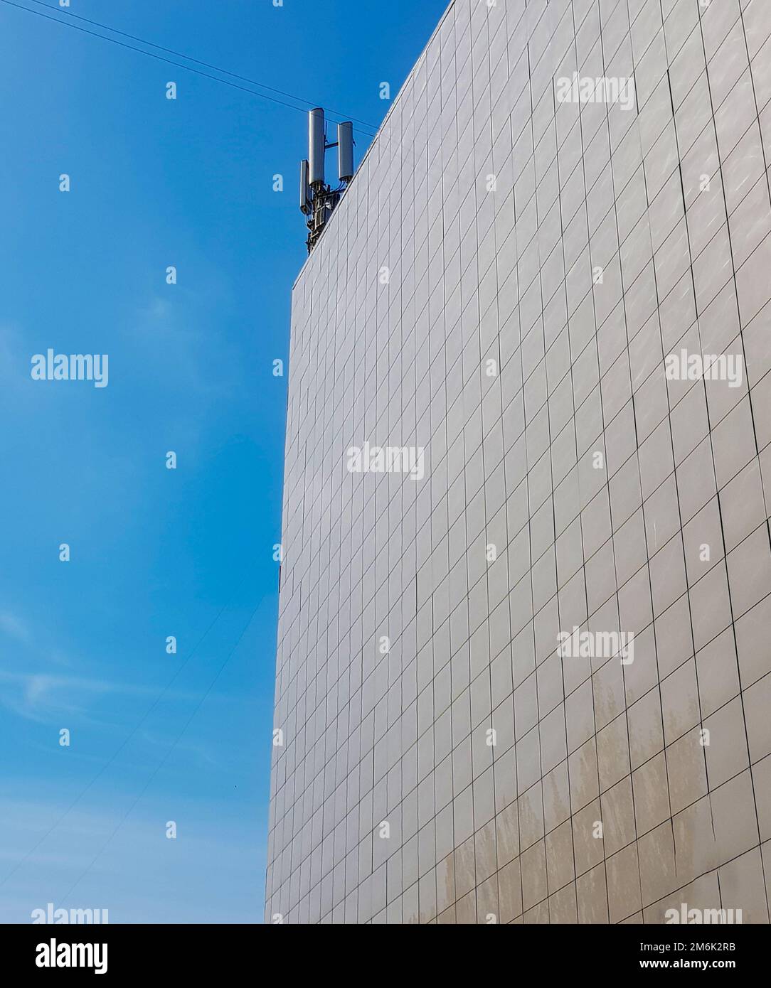 Die Außenwand eines modernen, mit Fliesen getäfelten Geschäftsgebäudes auf dem Dach ist mit modernen Antennen gegen den blauen Himmel ausgestattet Stockfoto