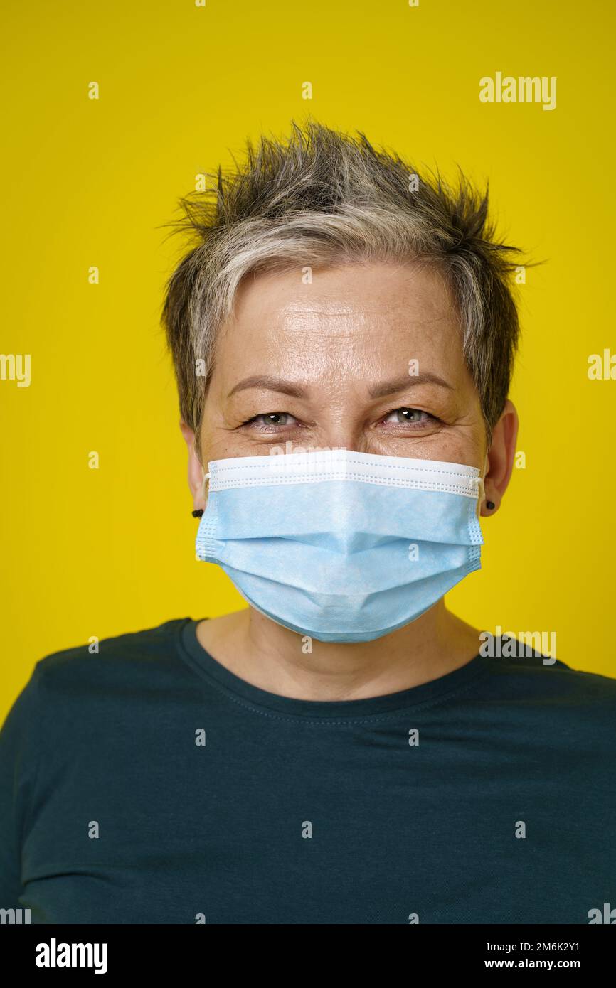 Glückliche Augen lächelnd grau kurze Haare Ärztin Frau trägt medizinische Gesichtsmaske Blick auf die Kamera trägt grüne Bluse isoliert auf y Stockfoto