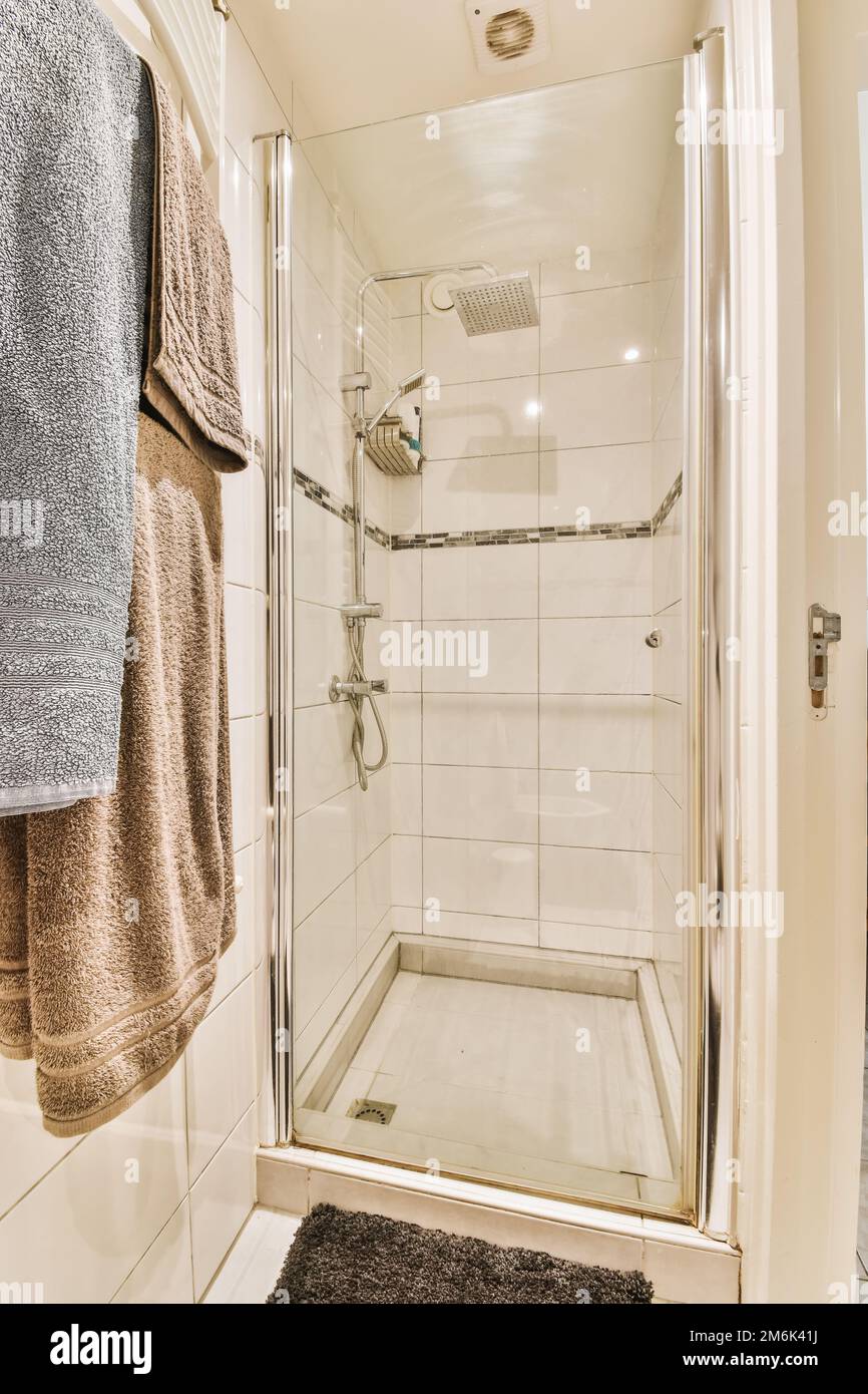Ein Badezimmer mit Handtüchern an der Wand und eine gläserne Duschtür in der Ecke, neben einem Handtuchhalter Stockfoto