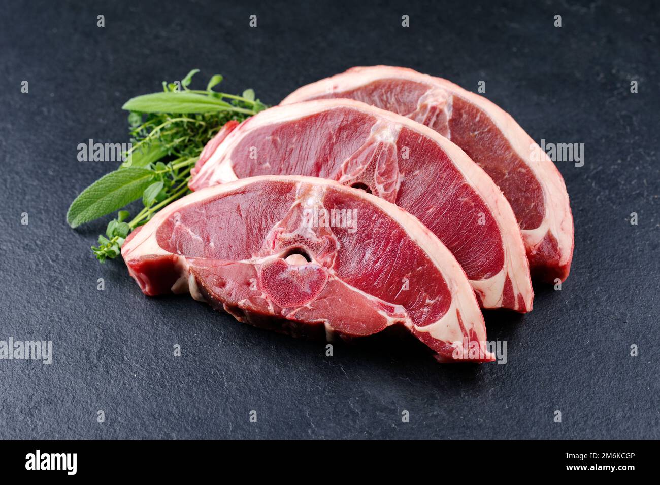 Rohes Lammsattelsteak mit Kräutern aus nächster Nähe auf einem schwarzen Designbrett mit Kopierbereich Stockfoto