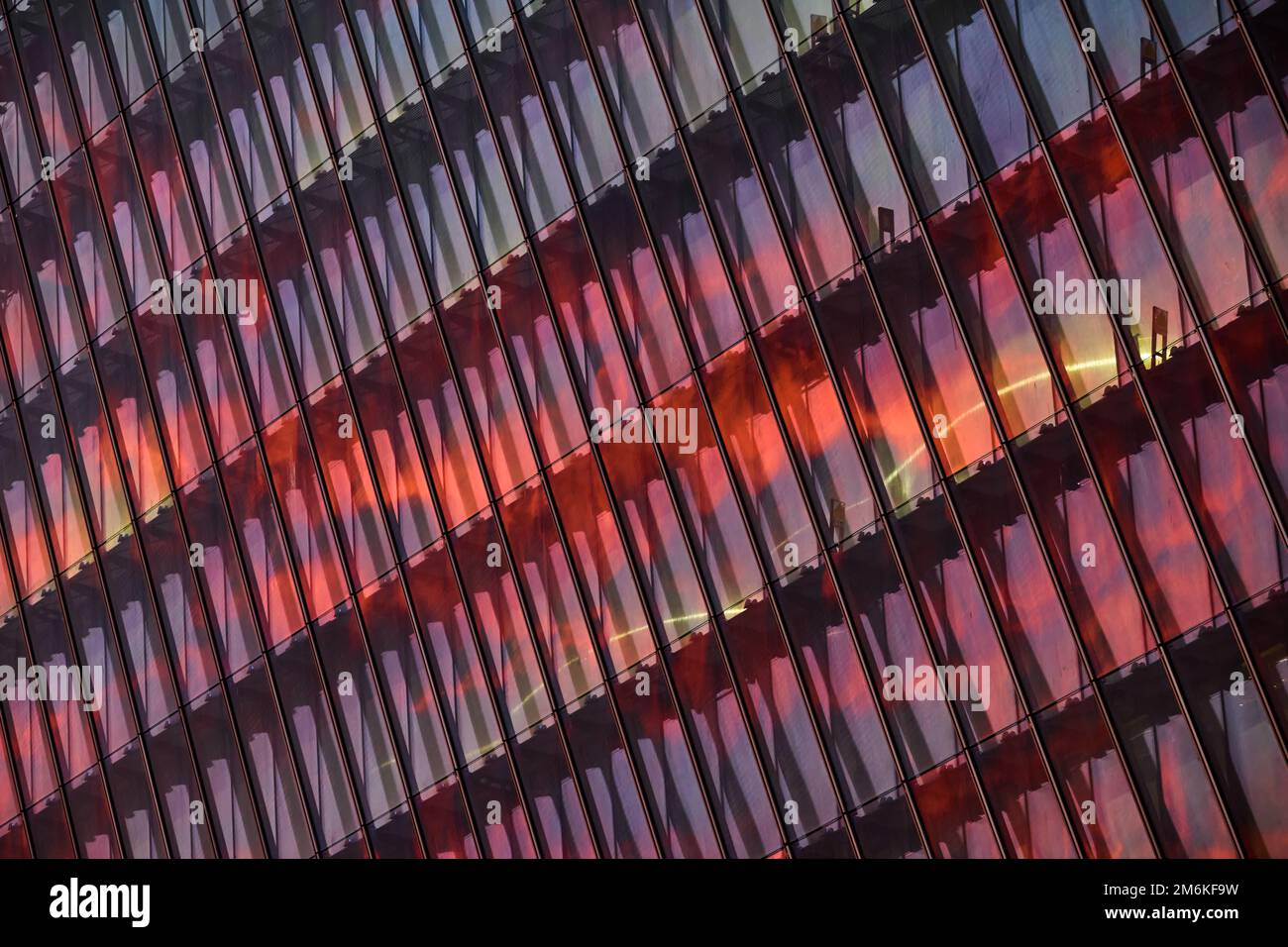 Die Glas- und Eisenfassade eines riesigen Wolkenkratzers bei Sonnenuntergang, Stahl, orange Farbe, Spiegelung der Sonne Stockfoto