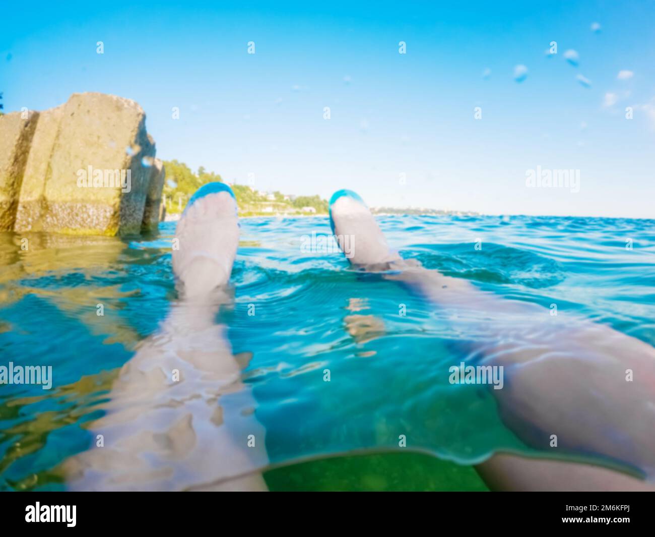 Ungeschickte Füße in Gummischuhen stehen vor dem Hintergrund der Meereslandschaft aus dem Wasser. Strandurlaub. Abkühlung in t Stockfoto
