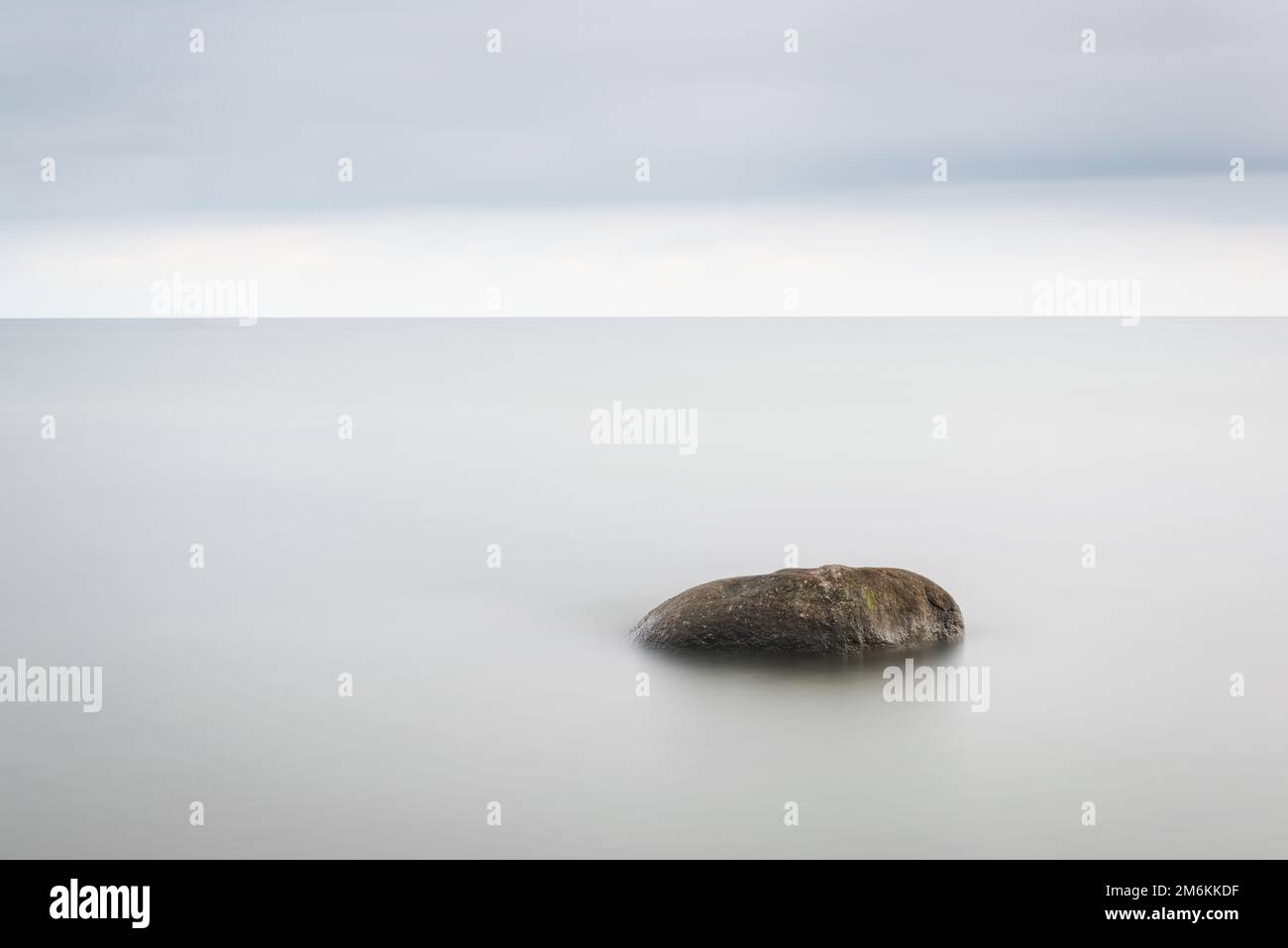 Das Meer wäscht die großen Steine gegen den rosa Sonnenuntergang. Die verwendete Technik - Langzeitbelichtung. Stockfoto