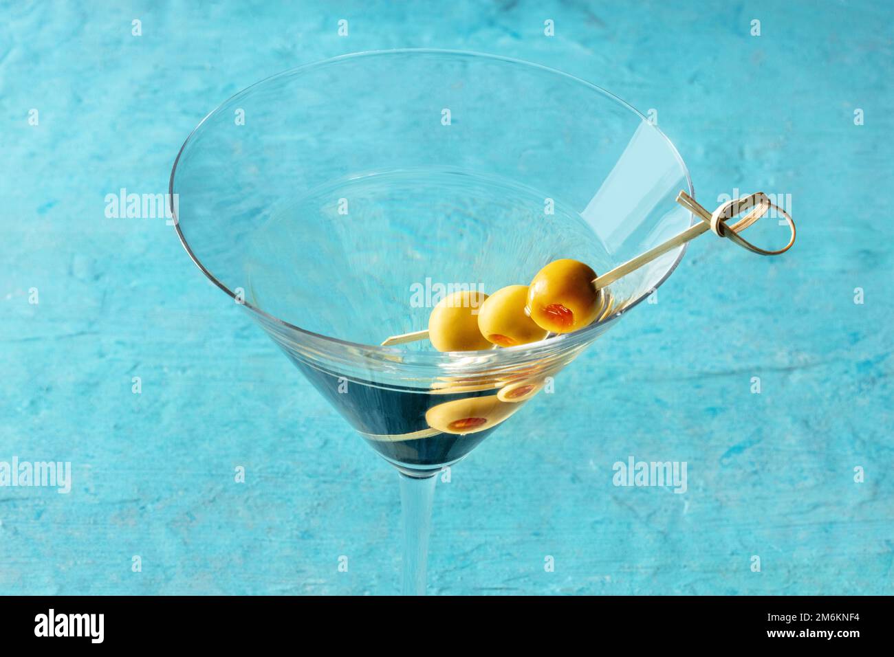 Martini, ein Glas mit scharfen Oliven auf einem Zahnstocher, auf blauem Hintergrund Stockfoto