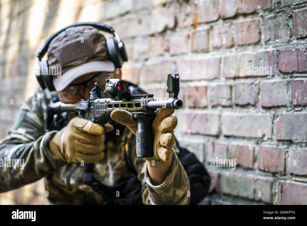 Ausbildungszyklus im Dienst für Zivilpolizeitruppen. Junger Mann mit Waffe, der bei fortgeschrittenen Schusswaffen seitlich neben einer Mauer steht Stockfoto