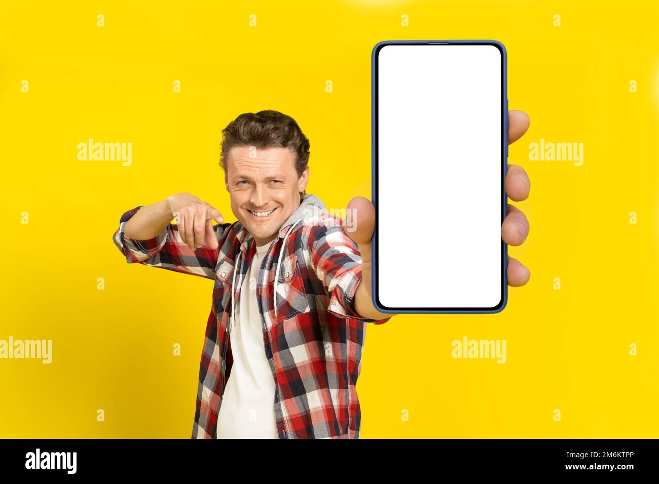 Sieh dir das an. Glücklicher, gutaussehender Mann, der auf ein riesiges Smartphone zeigt, mit weißem, leerem Bildschirm, rotes Karohemd trägt, Handydis Stockfoto