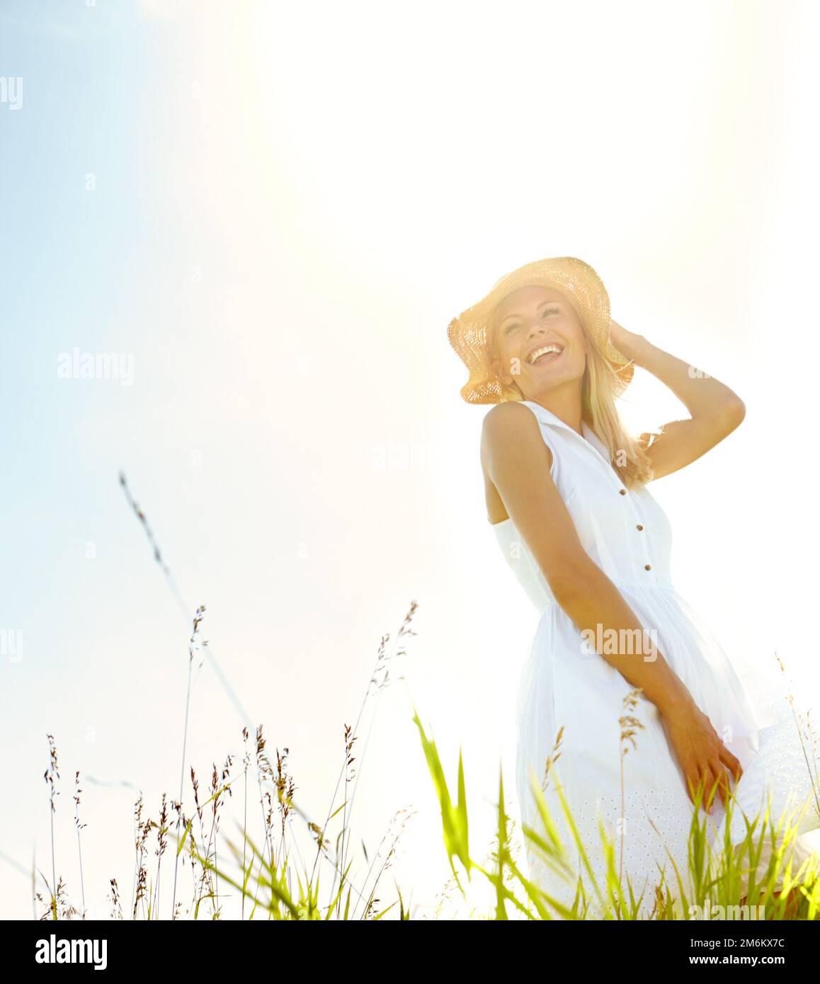 Genießen Sie die Ruhe der Natur. Eine wunderschöne, blonde Frau, die an einem warmen Sommertag auf einer Wiese steht und einen Sonnenhut trägt. Stockfoto