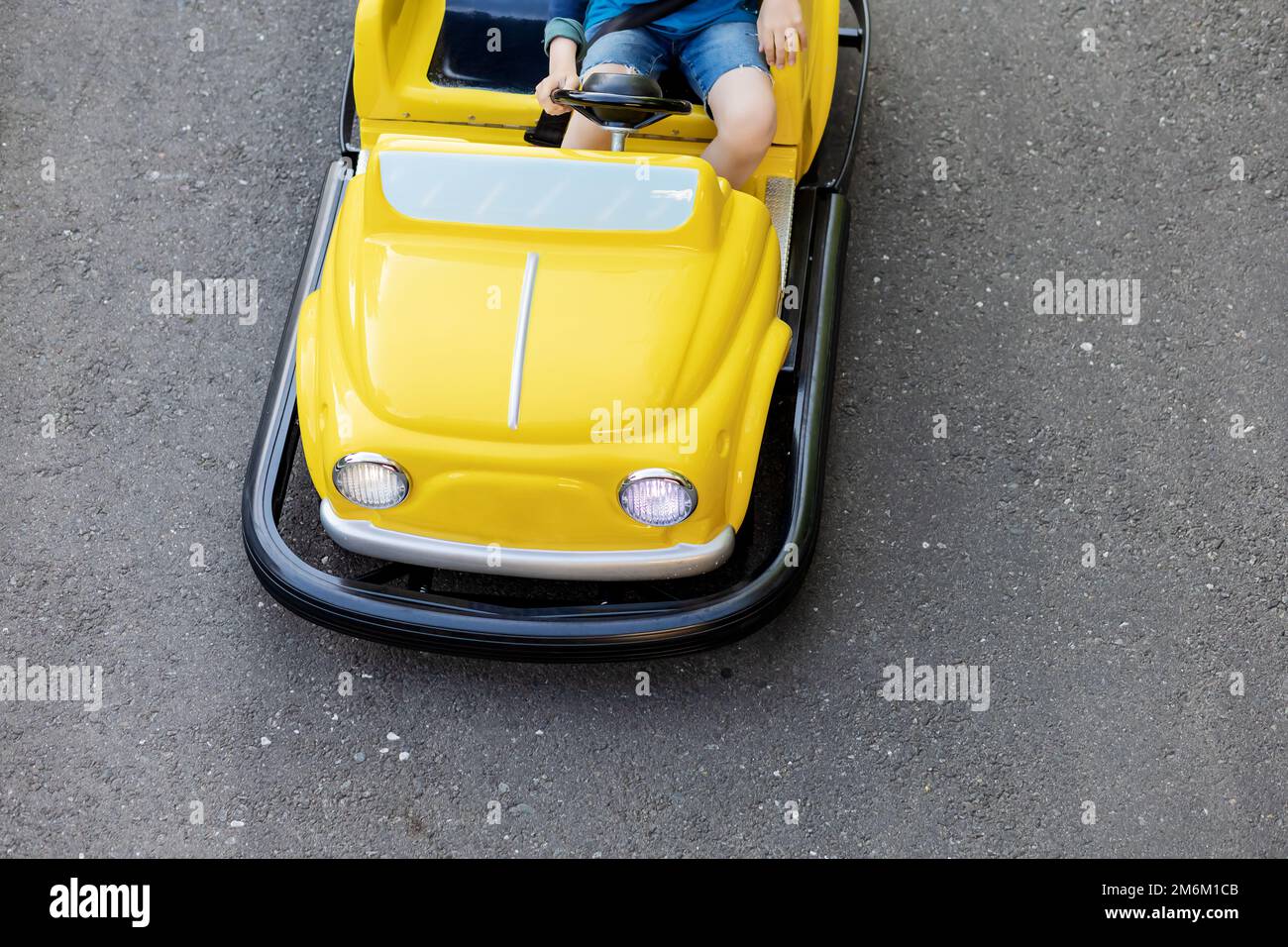Ein Kind fährt ein kleines gelbes Auto mit runden Scheinwerfern auf einer Asphaltstraße. Highway für Kinder im Vergnügungspark Stockfoto