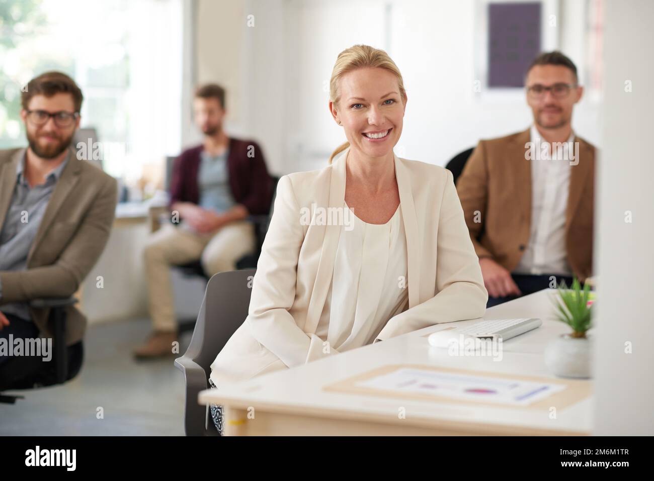 Ansprechende Kreative. Lächelnde kreative Frau mit Kollegen im Hintergrund. Stockfoto