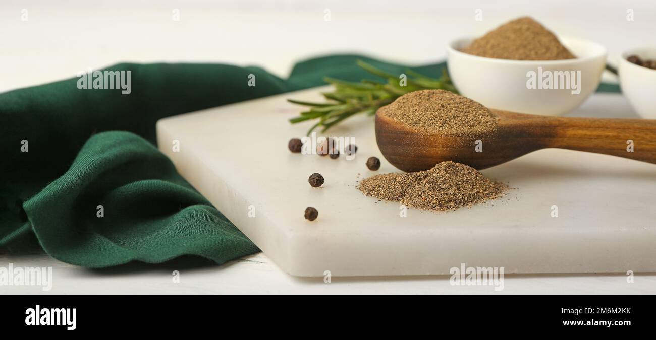 Löffel mit schwarzem Pfefferpulver auf einem hellen Tisch Stockfoto