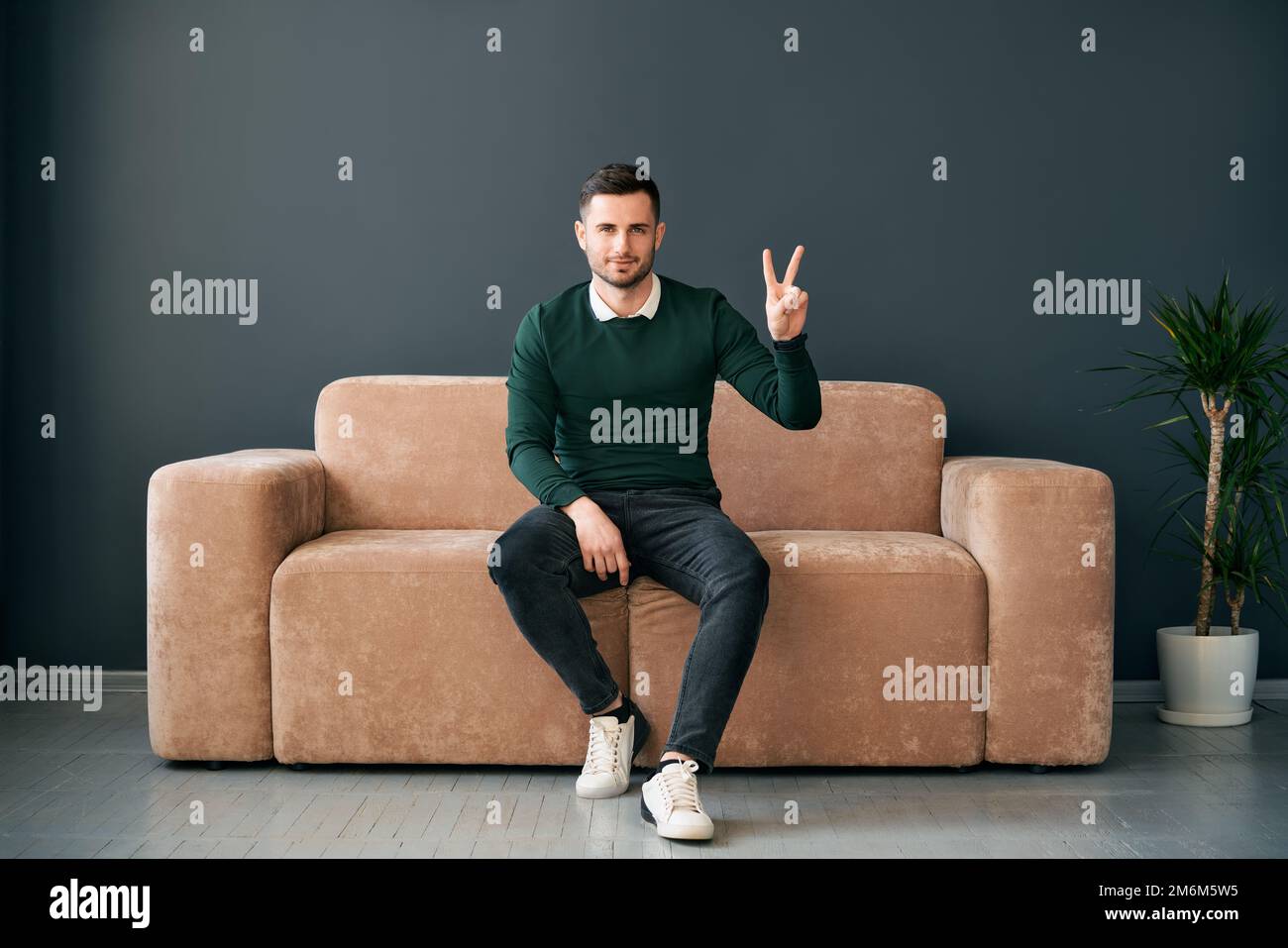 Trendiger Mann mit Handgeste V-Schild für Sieg oder Frieden sieht aus wie eine Kamera Stockfoto