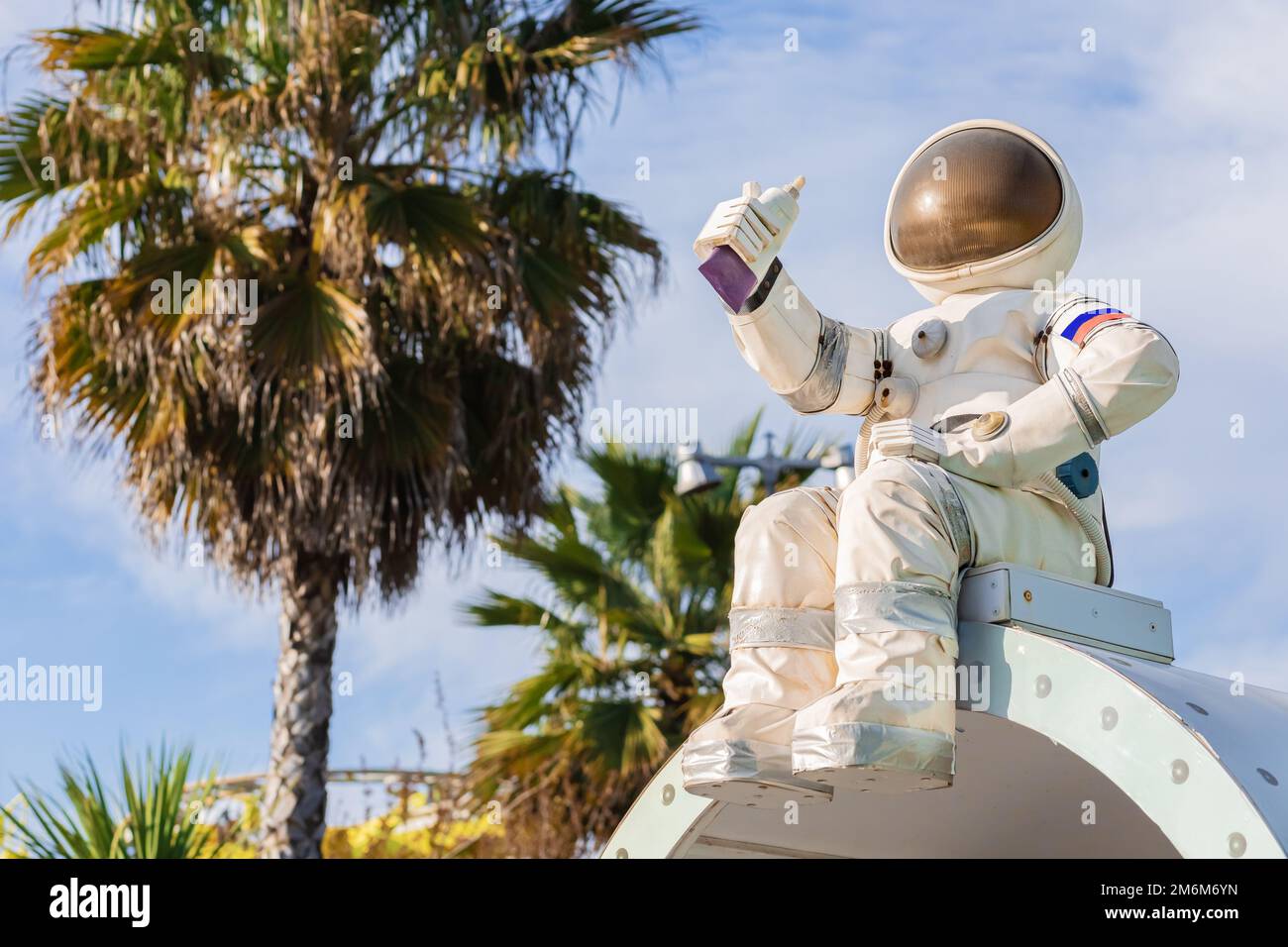Die Figur eines Astronauten in einem Raumanzug, der eine Tube Nahrung in der Hand hält, sitzt vor dem Hintergrund von Palmen und dem Himmel Stockfoto