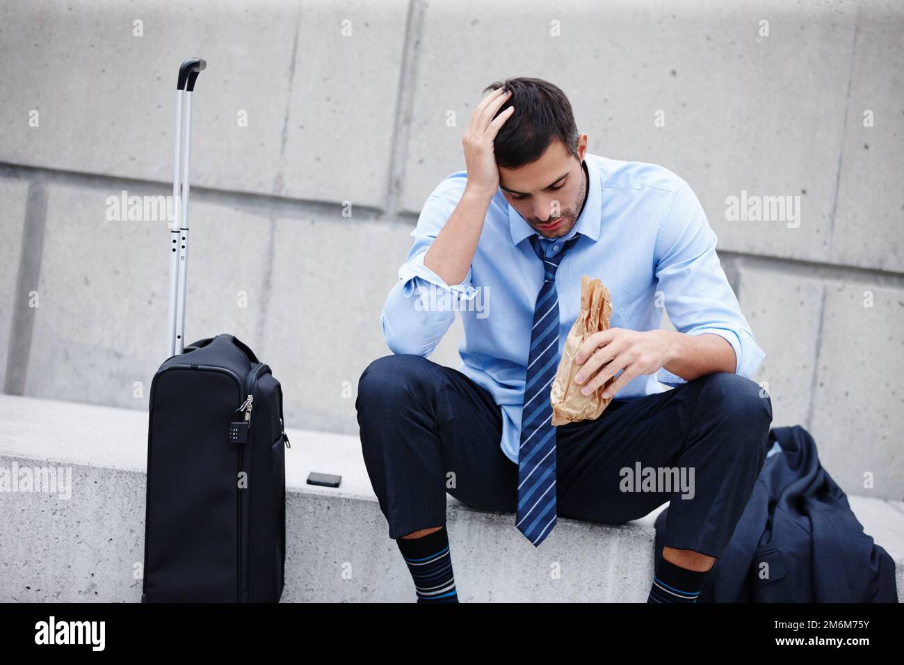 Er kämpft mit Einschränkungen. Ein junger Geschäftsmann, der draußen sitzt und trinkt, während er deprimiert aussieht. Stockfoto