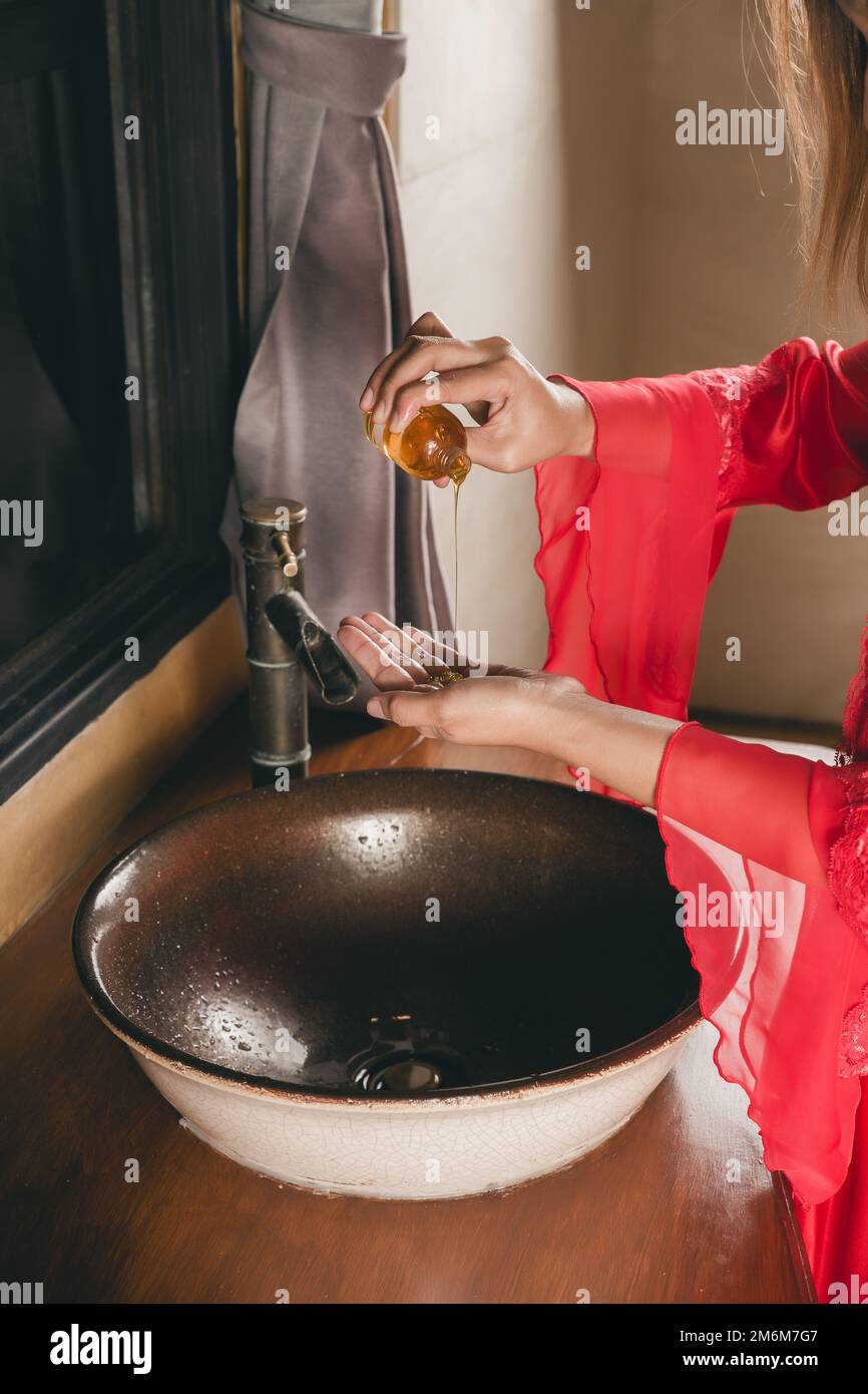 Eine Frau in einem roten Seidenmantel, die nachts Handgel aus der Flasche in die Hand gießt. Stockfoto