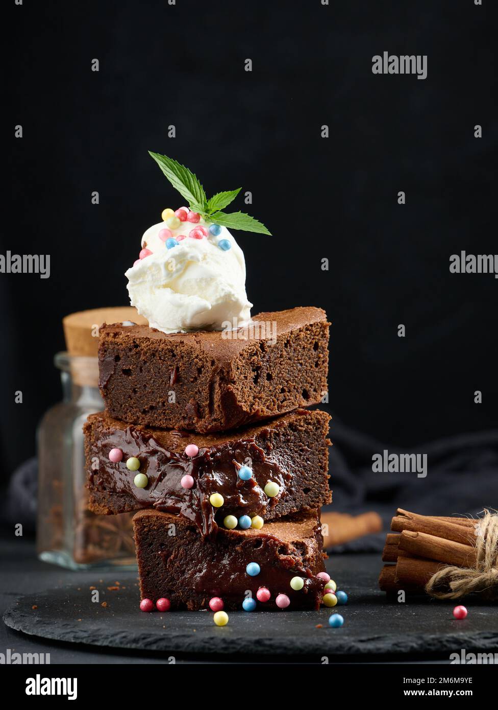 Gebackene Brownie-Schokoladenstückchen auf einem schwarzen Tisch, auf einer Kugel Eis Stockfoto