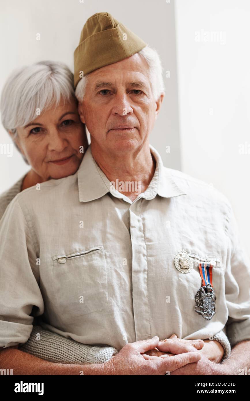 Er war immer mein Held. Eine ältere Frau, die ihren Mann von hinten umarmt, während er seine Armeeuniform trägt. Stockfoto