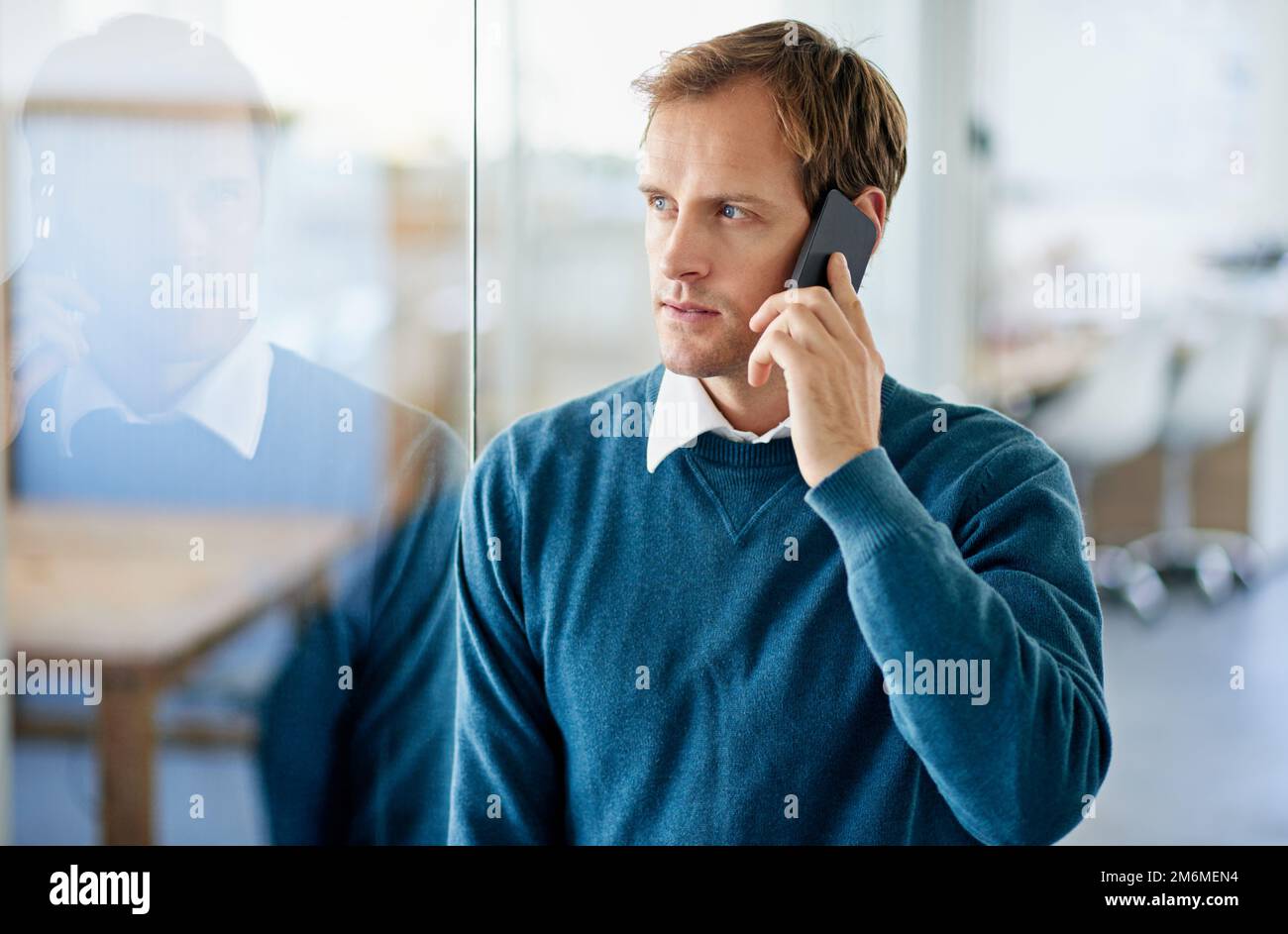 Ich höre, was du sagst. Ein gutaussehender Geschäftsmann, der mit seinem Handy im Büro spricht. Stockfoto