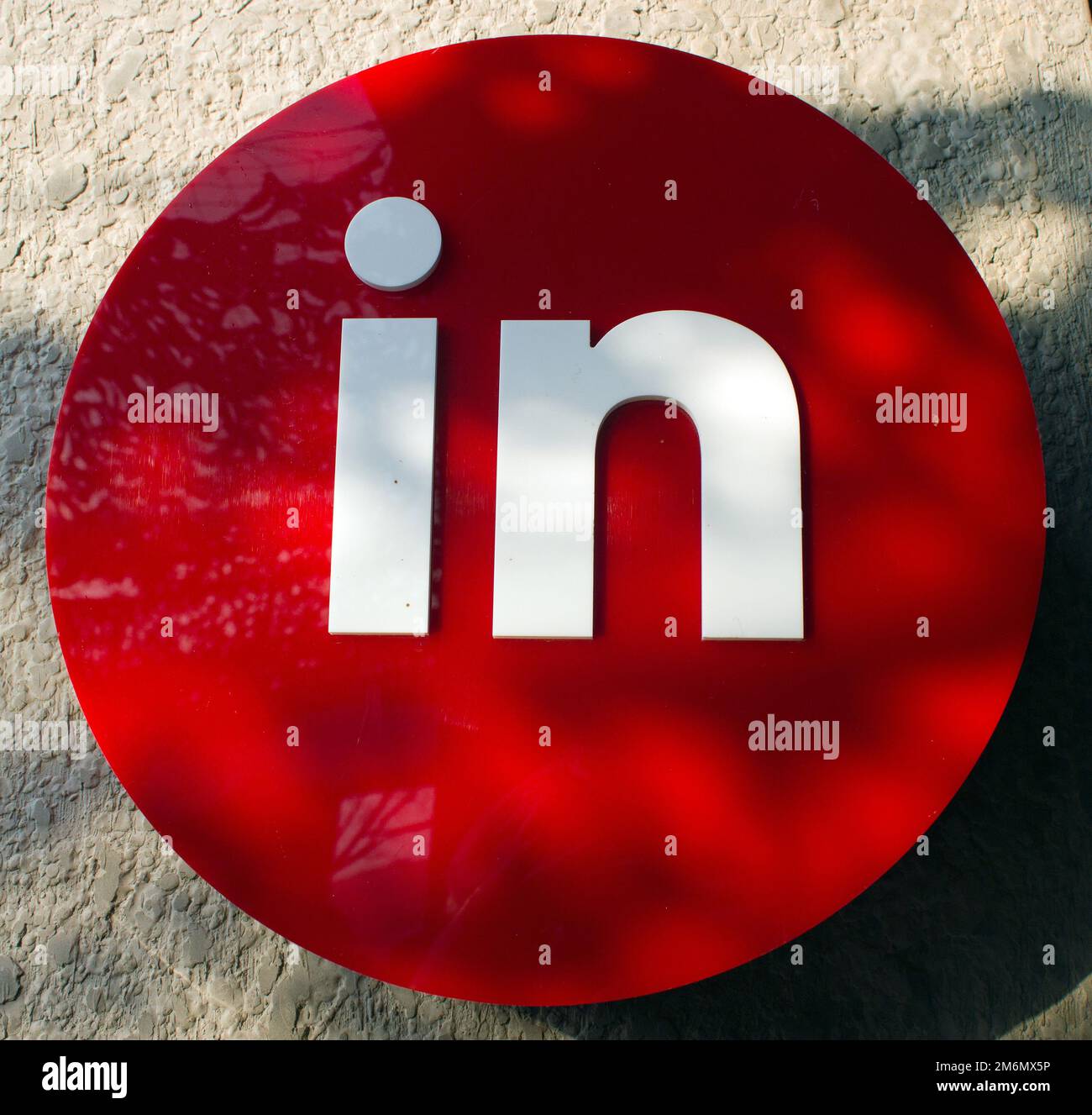 Weißes „in“-Schild auf blutrotem Hintergrund vor Beton, das den Weg in das Gebäude oder Geschäft zeigt Stockfoto