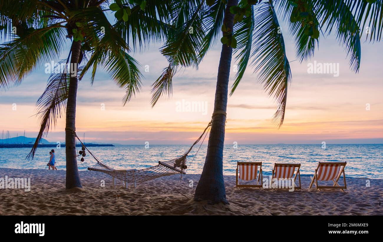 Hängematte und Liegestühle am Strand mit Palmen während des Sonnenuntergangs am Na Jomtien Beach Pattaya Thailand. Stockfoto