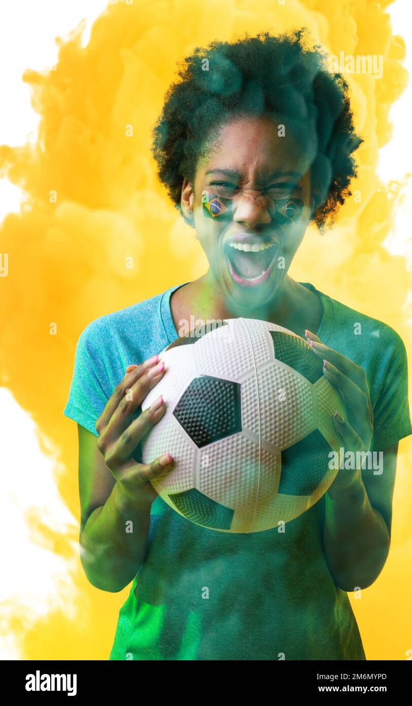 afrikanische amerikanische Fans mit brasilianischer Fahne und einem Ball, der auf rauchigem Hintergrund schreit Stockfoto