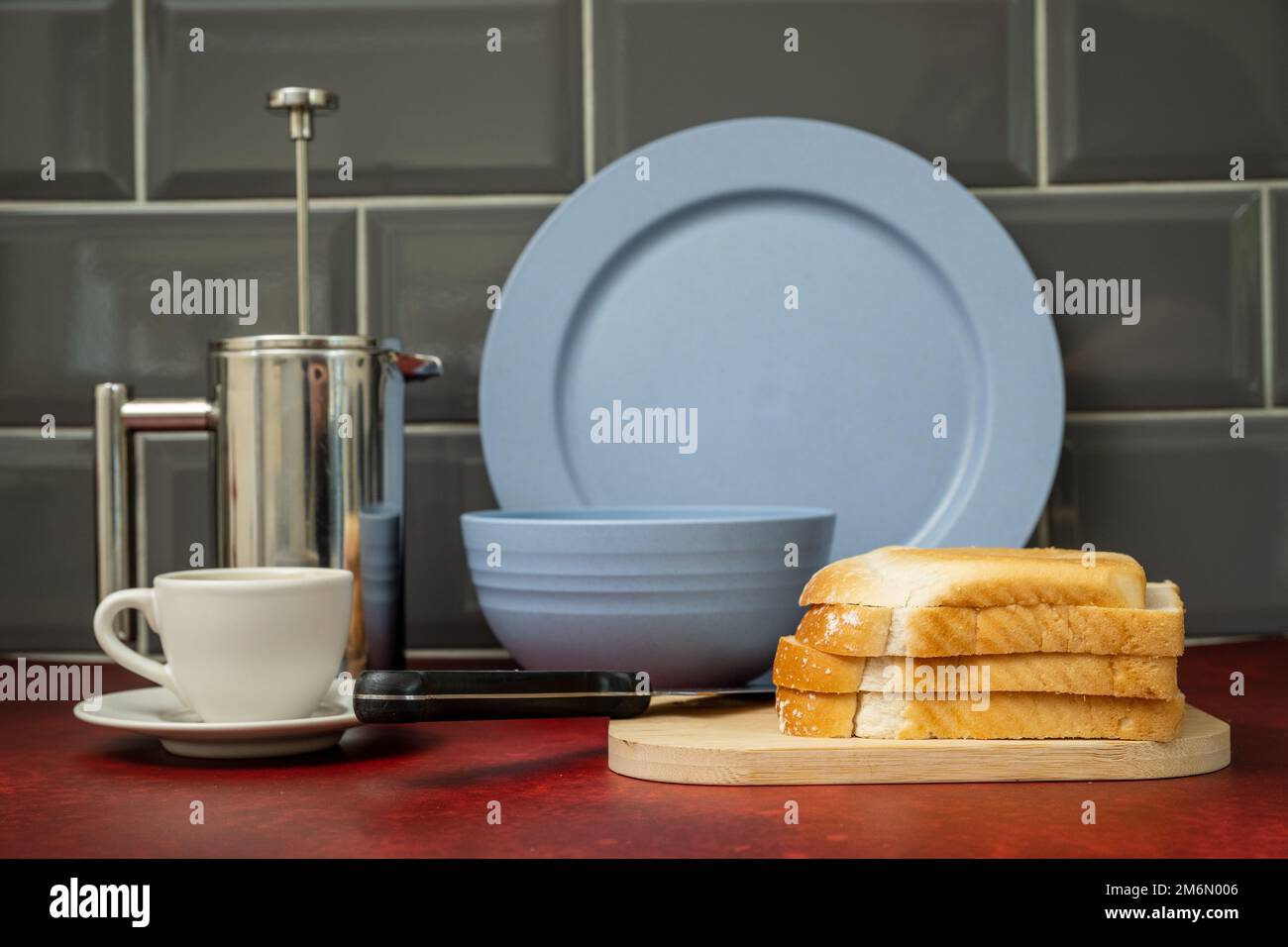 Espresso-Kaffeetasse und -Untertasse Edelstahl cafetiere schwarzes Edelstahlmesser auf Holzbrett mit frischem Brot blaues Abendset auf Rot Stockfoto