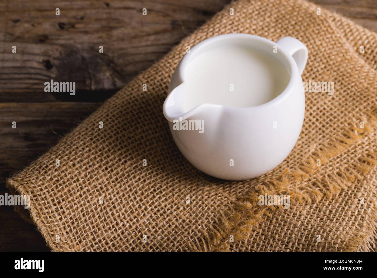 Milch im Krug auf Sackleinen am Holztisch, Platz kopieren Stockfoto