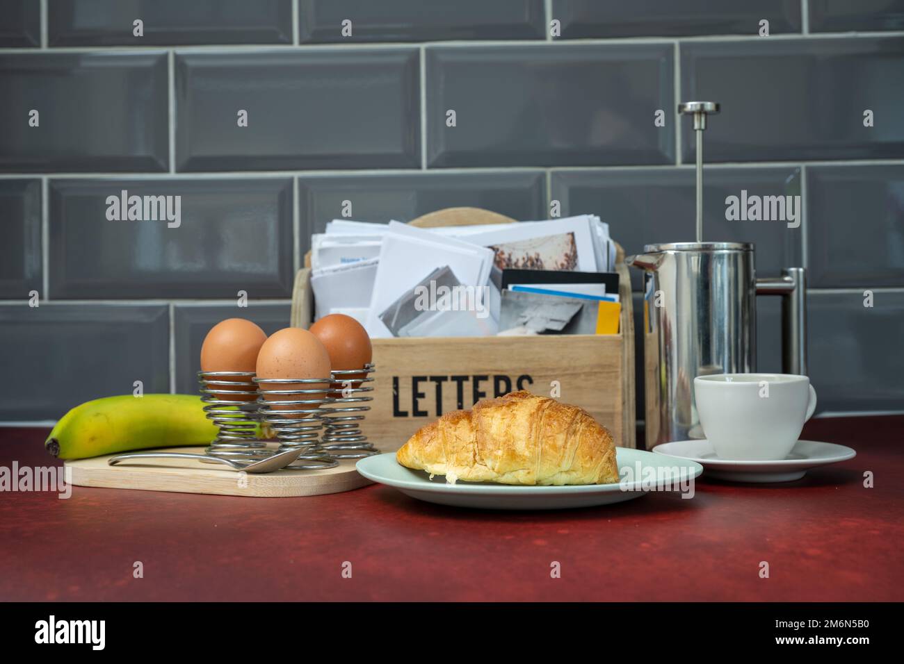Ausgewählter Fokus auf französischem Frühstückscroissant mit gekochten Eiern, Kaffeekanne und Tasse im Hintergrund auf einem roten Tisch Stockfoto