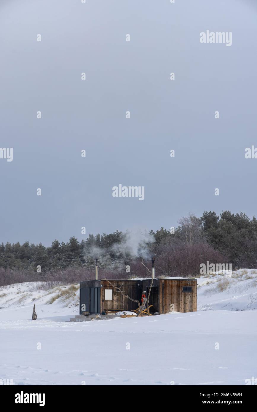 Hölzerne Sauna im Freien mit einem Rauch, der an einem wunderschönen kalten, verschneiten Wintertag an der Ostsee aus dem Kamin kommt. Wohlbefinden und gesunder Lebensstil. Stockfoto