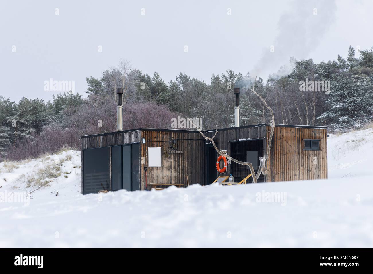 Hölzerne Sauna im Freien mit einem Rauch, der an einem wunderschönen kalten, verschneiten Wintertag an der Ostsee aus dem Kamin kommt. Wohlbefinden und gesunder Lebensstil. Stockfoto