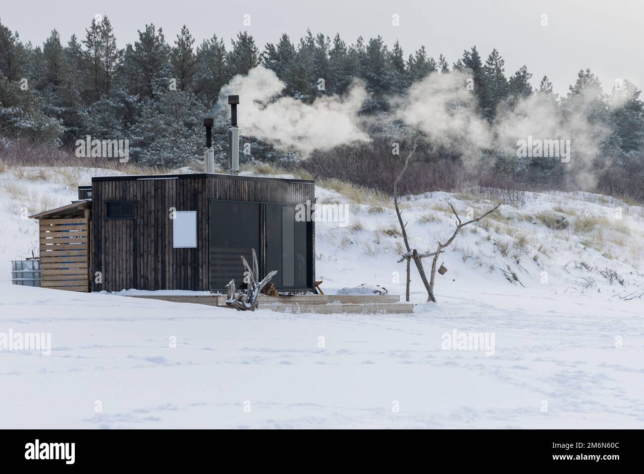 Hölzerne Sauna im Freien mit einem Rauch, der an einem wunderschönen kalten, verschneiten Wintertag an der Ostsee aus dem Kamin kommt. Wohlbefinden und gesunder Lebensstil. Stockfoto