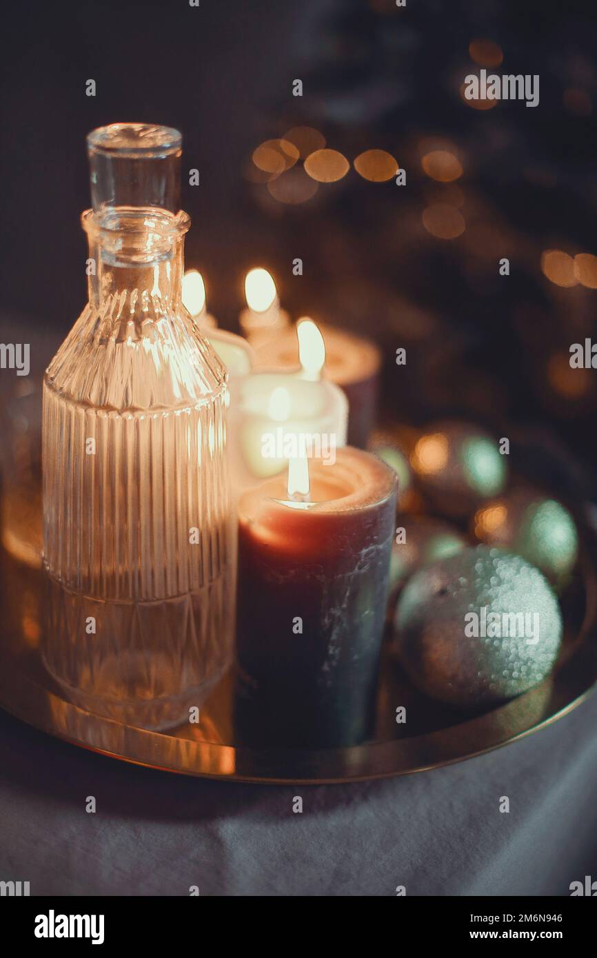 Silvester-Stillleben. Gläser und eine Karaffe aus transparentem Glas, Kerzen und goldener Weihnachtskugel Stockfoto