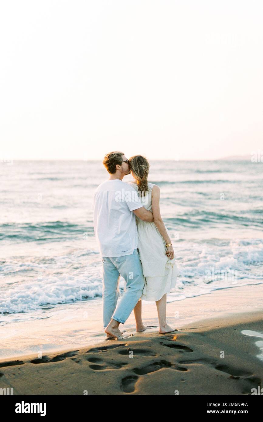 Ein Mann umarmt und küsst eine Frau auf dem Tempel, während er am Strand steht. Rückansicht Stockfoto