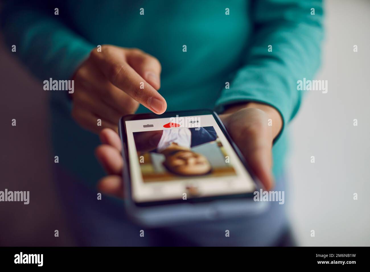 Mobiltelefon in den Händen einer Frau, die durch die Profile von Männern scrollt und den roten Herzknopf drückt. Stockfoto