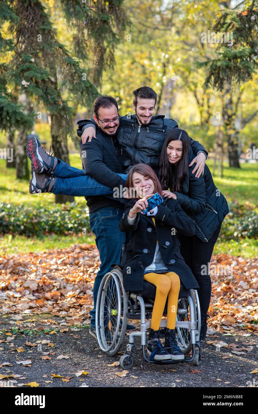 Eine Frau im Rollstuhl macht Selfie mit Freunden in einem Park Stockfoto