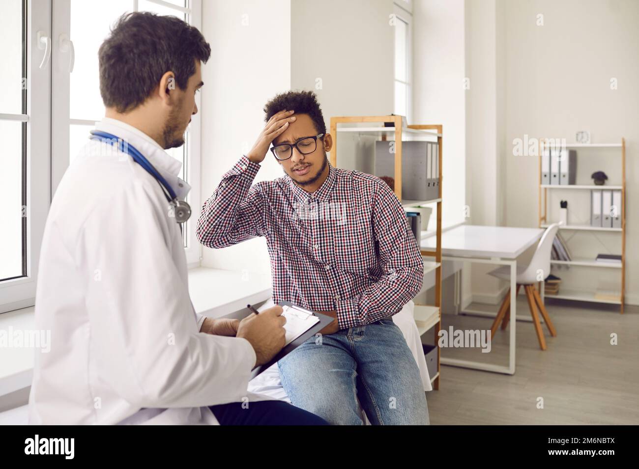 Junger dunkelhäutiger Mann klagt über Schwindel und Kopfschmerzen während der ärztlichen Untersuchung. Stockfoto