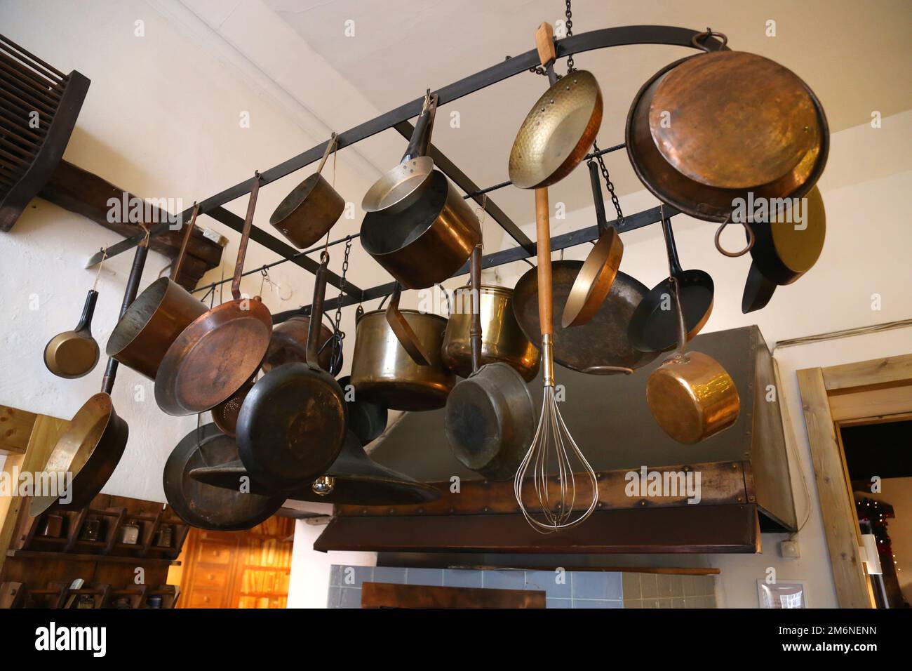 Antik aussehende Kupfer-, Messing- und eiserne Pfannen und Töpfe, die über dem Küchenherd hängen. Stockfoto