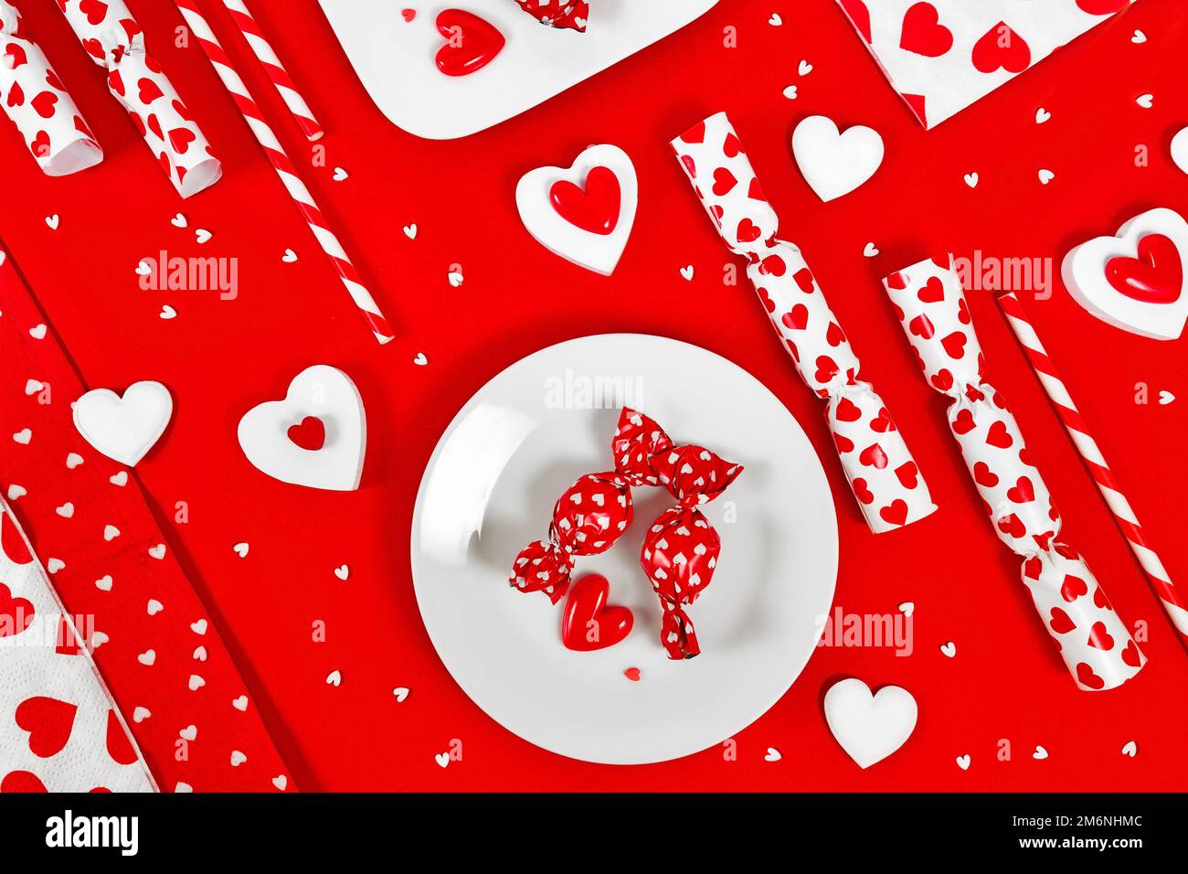 Dekoration zum Valentinstag mit Süßigkeiten, Herzschmuck und Zuckerstreuseln auf rotem Hintergrund Stockfoto