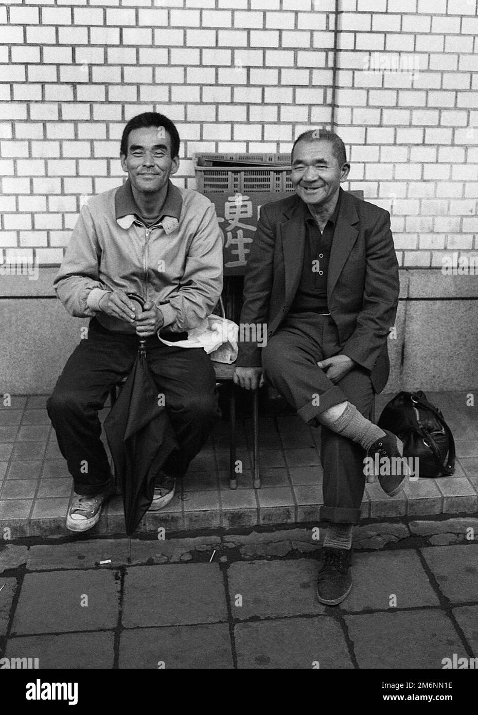 TOKIO JAPAN zwei Männer sitzen auf einer Bank und plaudern weiß und warten auf ihren Bus Stockfoto