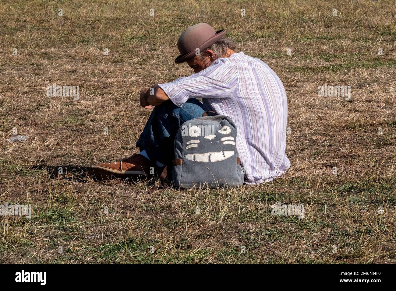 Ein Mann, der auf dem Rasen sitzt und einen Filzhut trägt Stockfoto