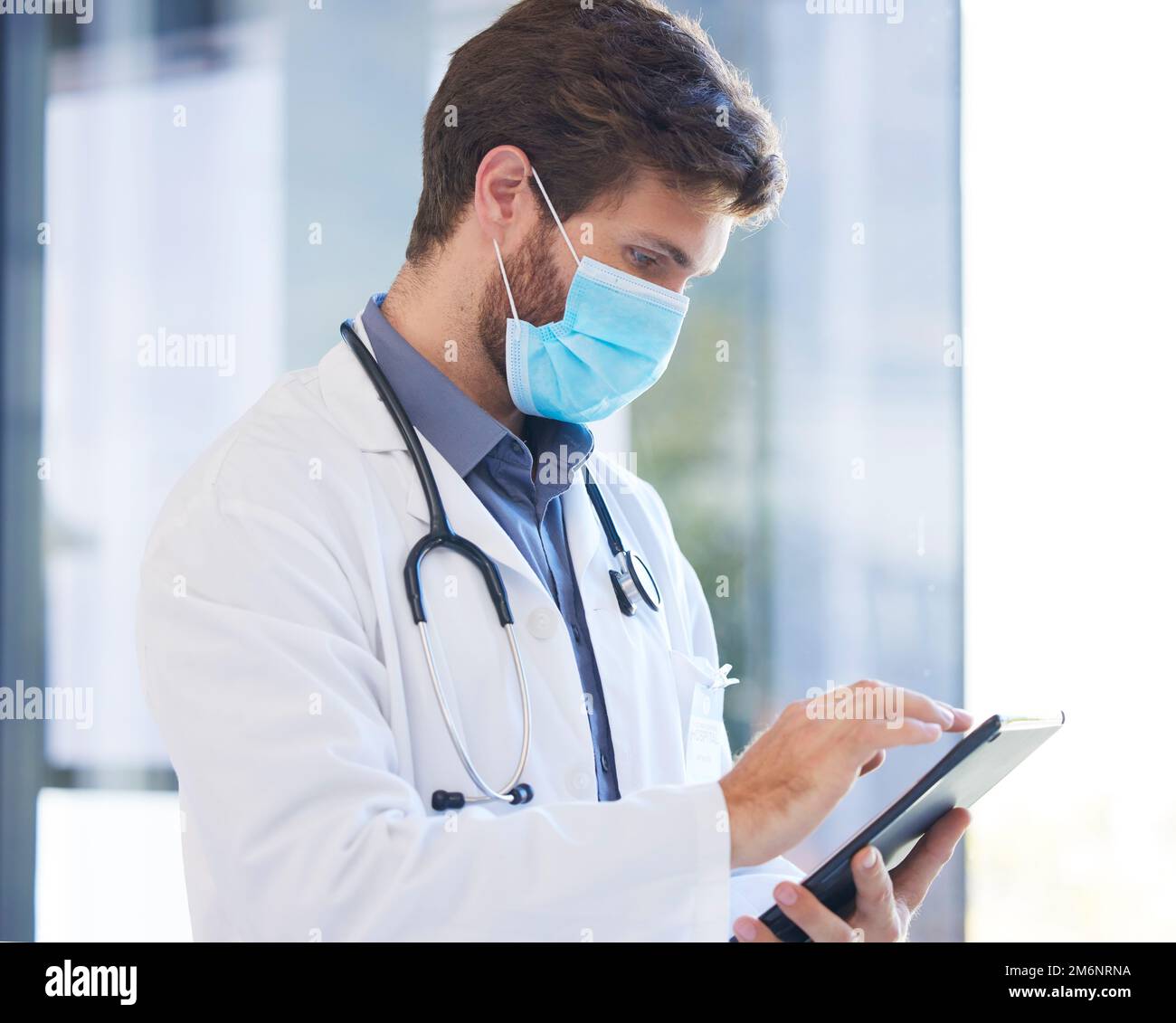Digitales Tablet, Gesichtsmaske und Arzt, der Forschung über Covid, Gesundheitswesen oder Pandemie in einem Krankenhaus. Fachkraft, Technologie und Mediziner Stockfoto
