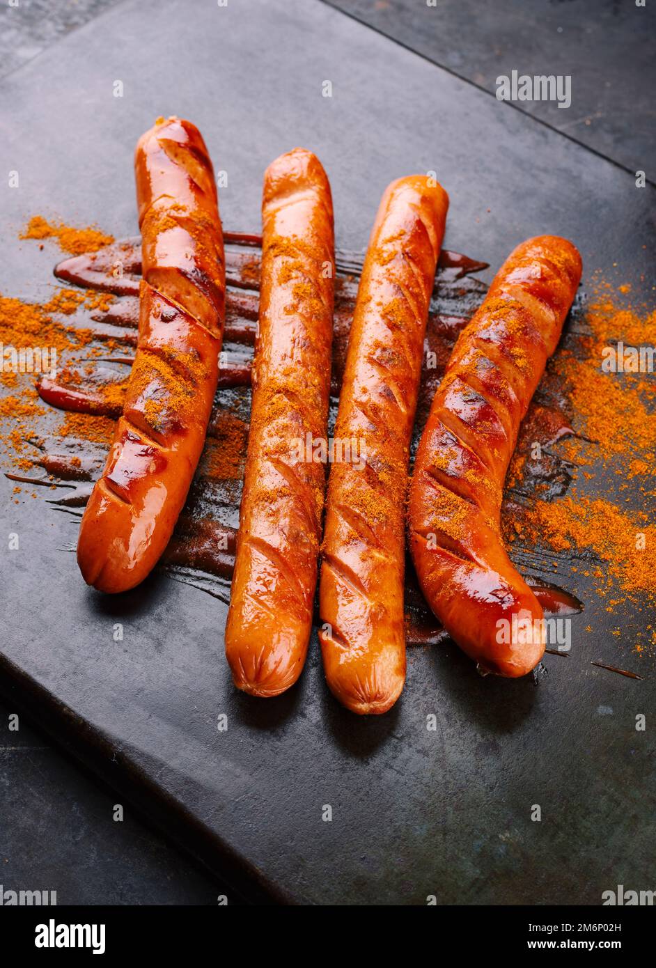 Traditionelle deutsche Barbecue-Currywurstwürste mit Ketchup und Currypulver, serviert als Nahaufnahme auf einem rustikalen schwarzen Brett Stockfoto