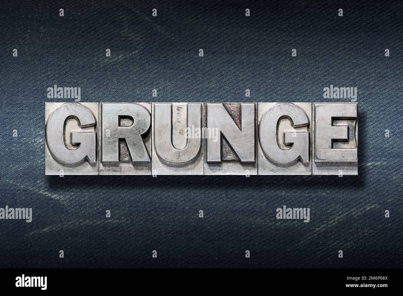Grunge-Wort aus metallischer Briefpresse auf dunklem Jeanshintergrund Stockfoto