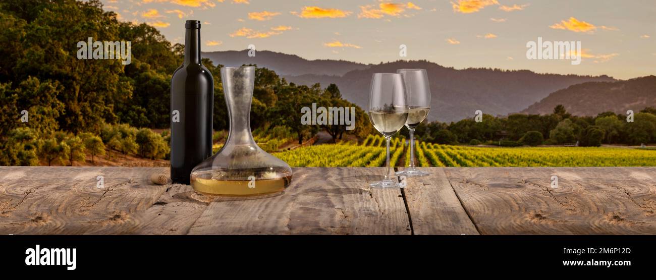 Flasche, Karaffe und zwei Gläser mit Weißwein stehen auf einem Holztisch über der wunderschönen Landschaft mit Feldern und Wäldern. Sommerzeit Stockfoto