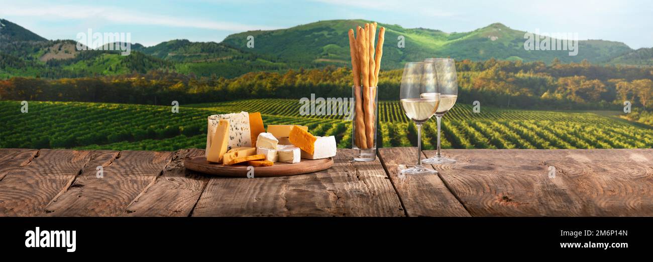 Zwei Gläser köstlicher Weißwein mit Käseplatte als Vorspeise stehen auf einem Holztisch. Schöne Aussicht auf die Felder im Sommer Stockfoto