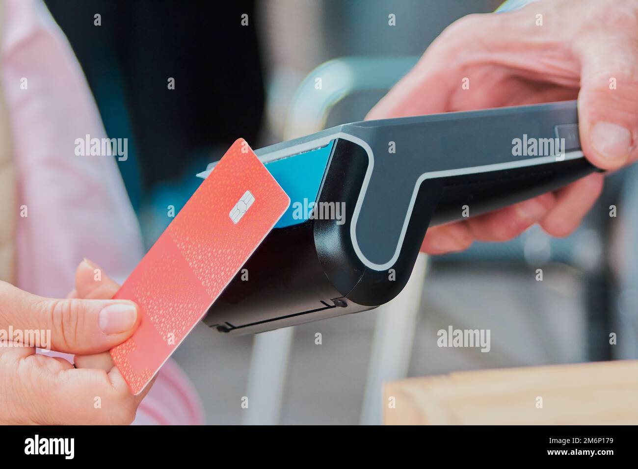 Frau, die mit einer Erwachsenenkarte an einem drahtlosen, kontaktlosen elektronischen Kartenzahlterminal bezahlt, das von einem Mann gehalten wird. Stockfoto
