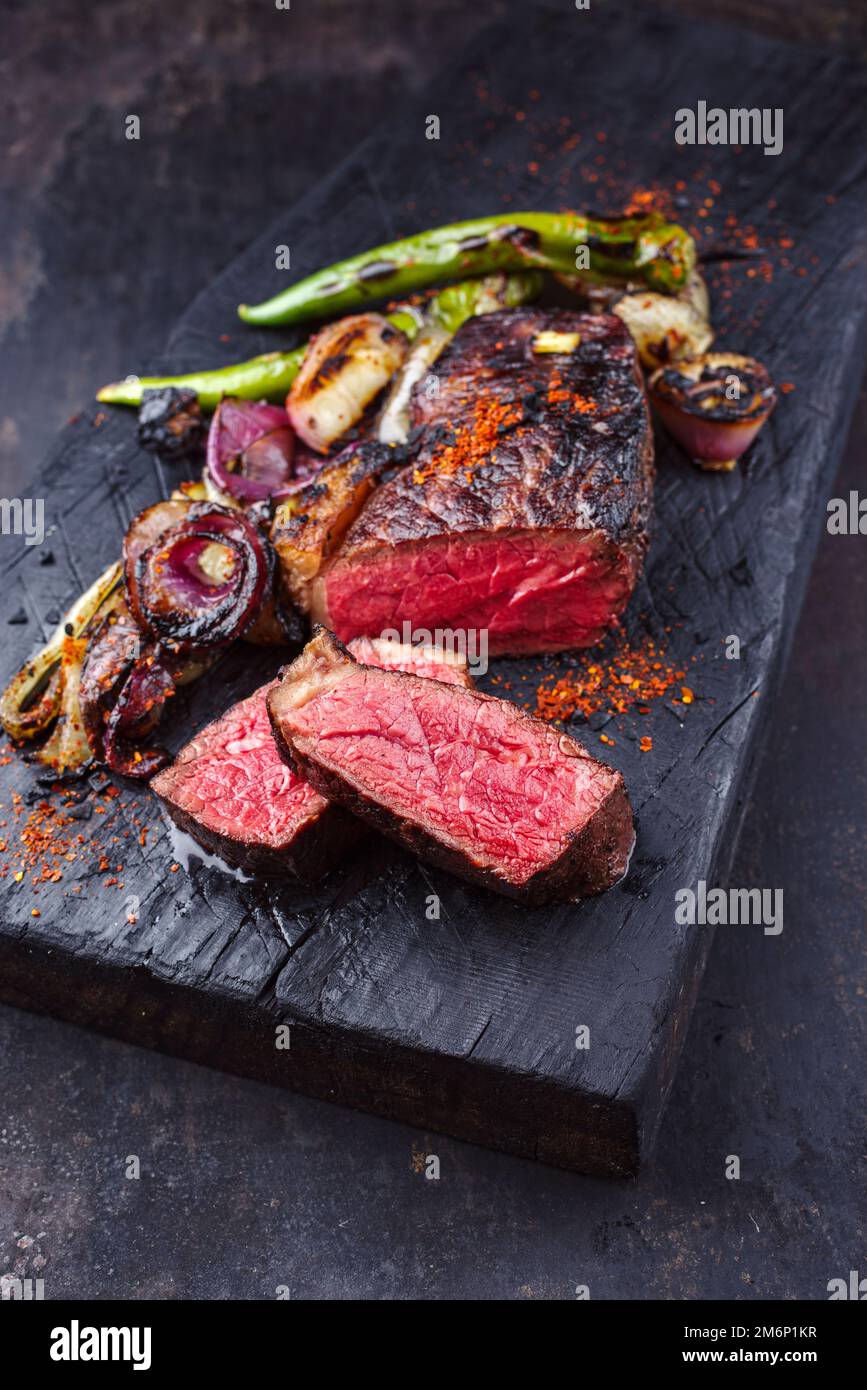 Barbecue trockenes, gereiftes Wagyu Roast Beef Steak mit BBQ Chili und Zwiebelringen serviert als Nahaufnahme auf einem verkohlten schwarzen Holzbrett Stockfoto