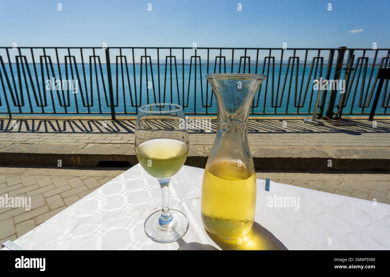 Weißwein auf dem Tisch an einem sonnigen Tag mit Meer- und Himmelshintergrund in Syrakus, Sizilien, Italien Stockfoto