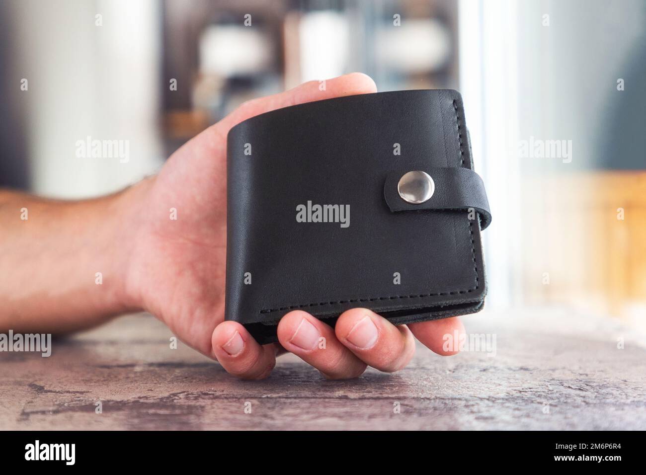Die Hand eines Mannes hält die handgemachte schwarze Ledertasche. Werbung für Handwerkeraccessoires, Nahaufnahme. Elegantes, modisches Produkt. Stockfoto