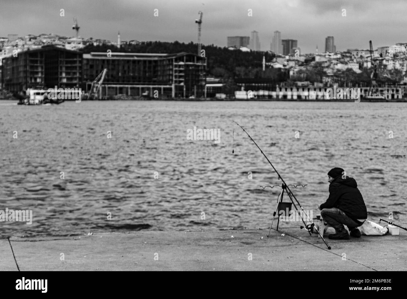Ein Mann, der versucht, gegen den Blick auf die schwarz-weiße Stadt in balat Istanbul in der türkei zu fischen Stockfoto